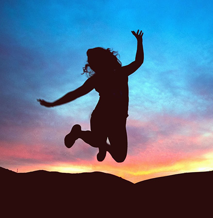 woman jumping outside with sun setting in background after trauma recovery therapy.