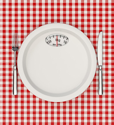 a scale as a plate between a knife and fork illustrating diet as a four letter word.